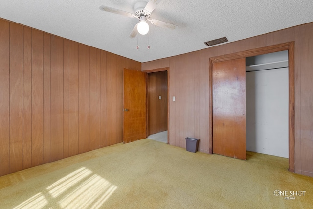 unfurnished bedroom featuring light carpet, wooden walls, ceiling fan, a textured ceiling, and a closet