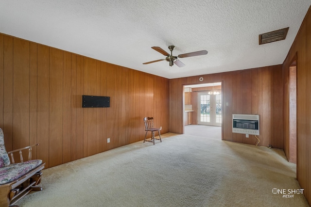 unfurnished living room with wood walls, ceiling fan, a textured ceiling, light colored carpet, and heating unit