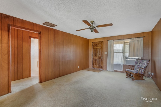 unfurnished room with light carpet, a textured ceiling, ceiling fan, wooden walls, and cooling unit