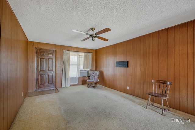 unfurnished room with ceiling fan, wood walls, cooling unit, light colored carpet, and a textured ceiling