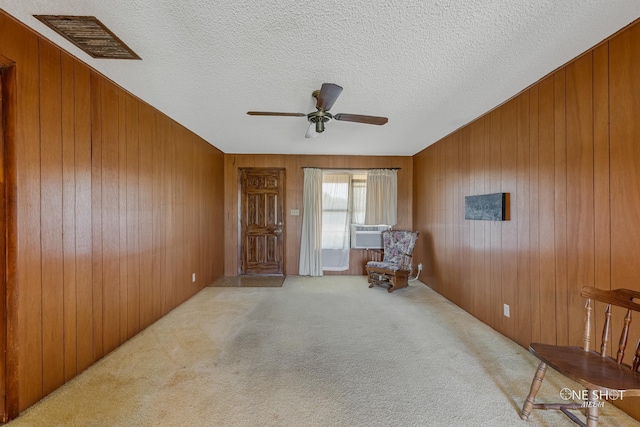 sitting room with ceiling fan, wood walls, light colored carpet, and a textured ceiling