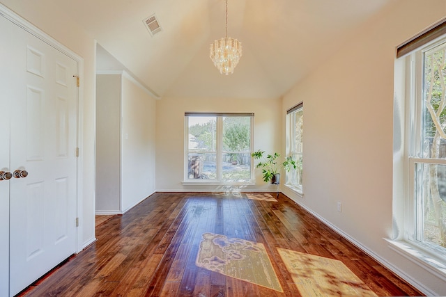 empty room with an inviting chandelier, a wealth of natural light, vaulted ceiling, and dark hardwood / wood-style floors