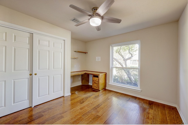 unfurnished office with light wood-type flooring, built in desk, and ceiling fan