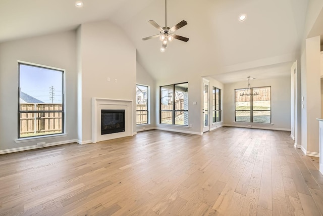 unfurnished living room featuring light hardwood / wood-style flooring, high vaulted ceiling, and ceiling fan with notable chandelier