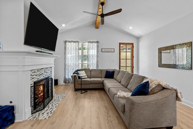 living room featuring a tiled fireplace, ceiling fan, light hardwood / wood-style flooring, and vaulted ceiling with beams