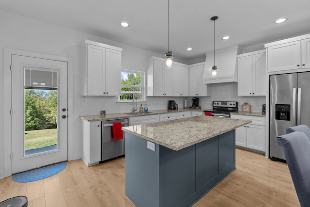 kitchen with a center island, sink, appliances with stainless steel finishes, decorative light fixtures, and white cabinetry