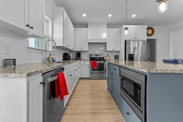 kitchen with pendant lighting, white cabinets, sink, decorative backsplash, and stainless steel appliances