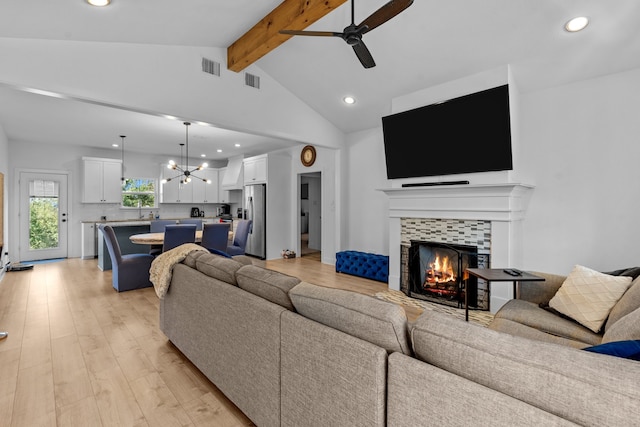 living room featuring a tile fireplace, light wood-type flooring, ceiling fan with notable chandelier, and vaulted ceiling with beams