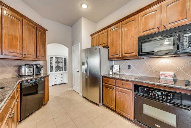 kitchen with decorative backsplash, black appliances, dark stone counters, and light tile patterned floors