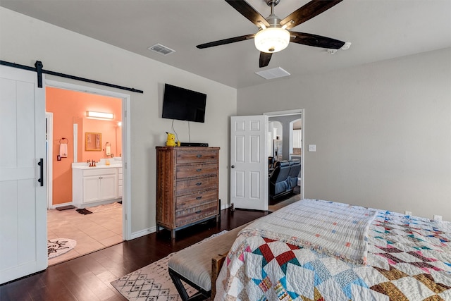 bedroom featuring ensuite bath, a barn door, dark hardwood / wood-style floors, and ceiling fan