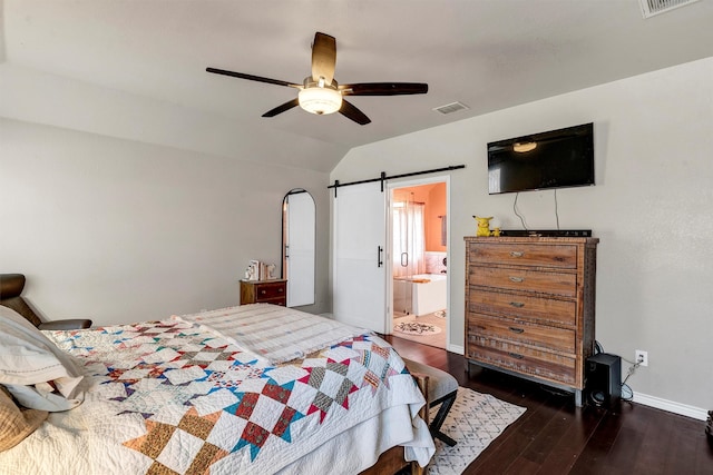 bedroom with a barn door, ceiling fan, vaulted ceiling, connected bathroom, and dark wood-type flooring