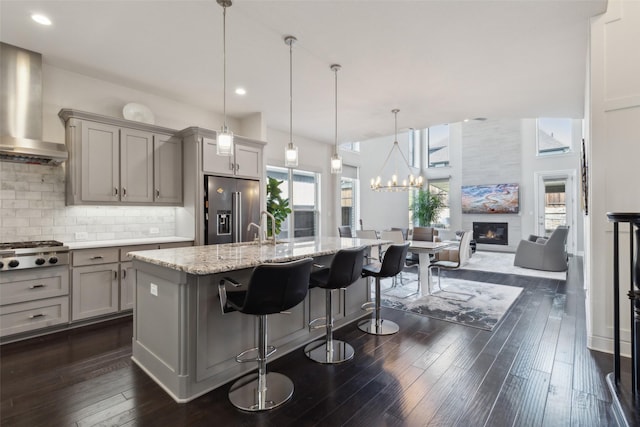 kitchen with appliances with stainless steel finishes, a kitchen breakfast bar, gray cabinets, a kitchen island with sink, and range hood