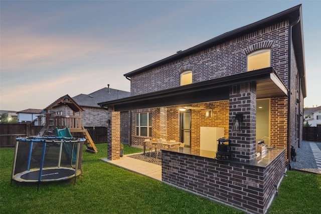 back house at dusk featuring a yard, a playground, a patio area, and a trampoline