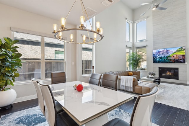 dining room with dark hardwood / wood-style floors, ceiling fan with notable chandelier, and a tile fireplace