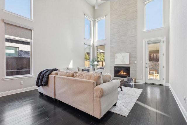 living room featuring a tile fireplace, a towering ceiling, and dark wood-type flooring