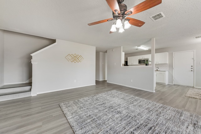 unfurnished living room with light hardwood / wood-style flooring, a textured ceiling, and ceiling fan