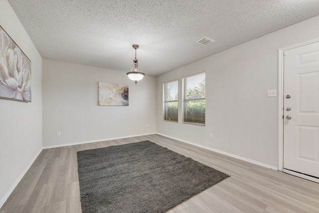 unfurnished dining area with a textured ceiling and light hardwood / wood-style flooring