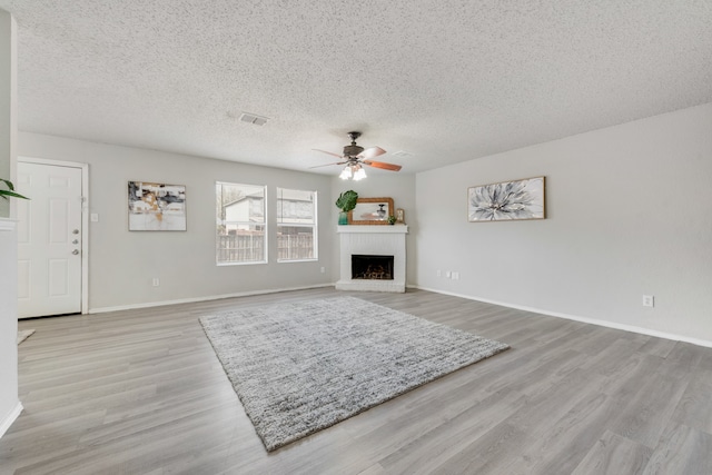 living room with a brick fireplace, a textured ceiling, light wood-type flooring, and ceiling fan