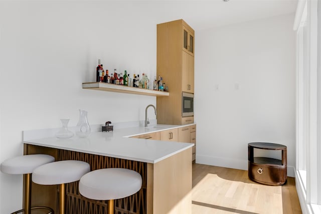 bar featuring stainless steel microwave, light brown cabinetry, light hardwood / wood-style flooring, and sink