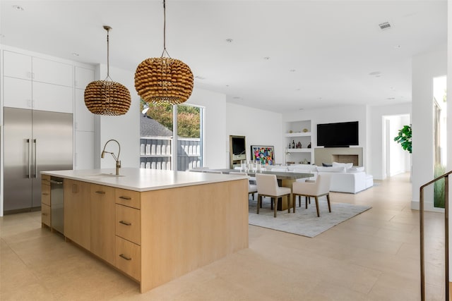 kitchen with a kitchen island with sink, light brown cabinets, sink, appliances with stainless steel finishes, and built in shelves