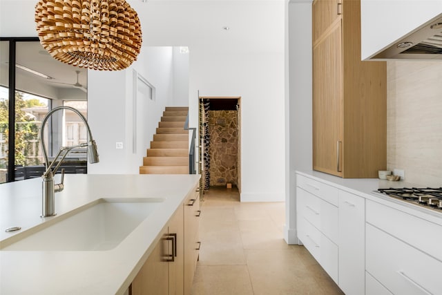 kitchen with sink, white gas stovetop, white cabinetry, range hood, and light tile patterned floors