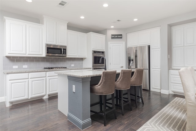 kitchen featuring an island with sink, backsplash, white cabinets, appliances with stainless steel finishes, and dark hardwood / wood-style flooring