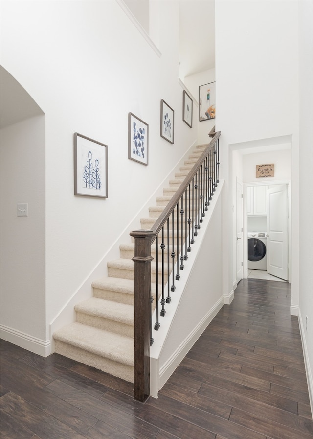 stairway with hardwood / wood-style floors, a towering ceiling, and washer / clothes dryer