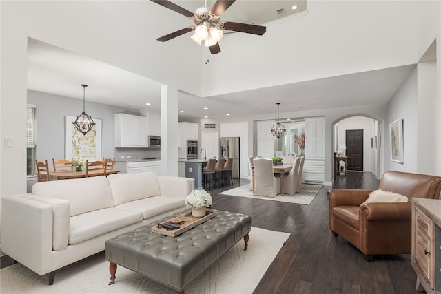 living room with a towering ceiling, ceiling fan, dark wood-type flooring, and a wealth of natural light