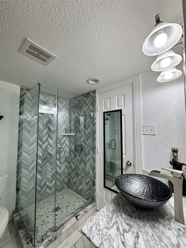 bathroom featuring a textured ceiling, toilet, a shower with shower door, and sink