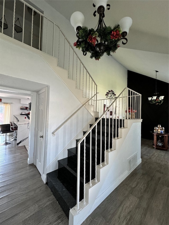 stairway with hardwood / wood-style flooring, high vaulted ceiling, and an inviting chandelier