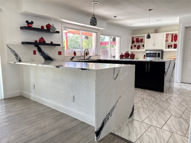 kitchen featuring white cabinetry, a center island, sink, pendant lighting, and a textured ceiling