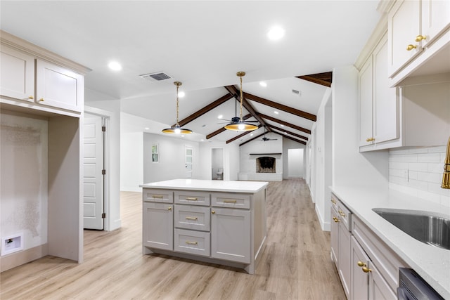 kitchen featuring ceiling fan, stainless steel dishwasher, light wood-type flooring, vaulted ceiling with beams, and a fireplace