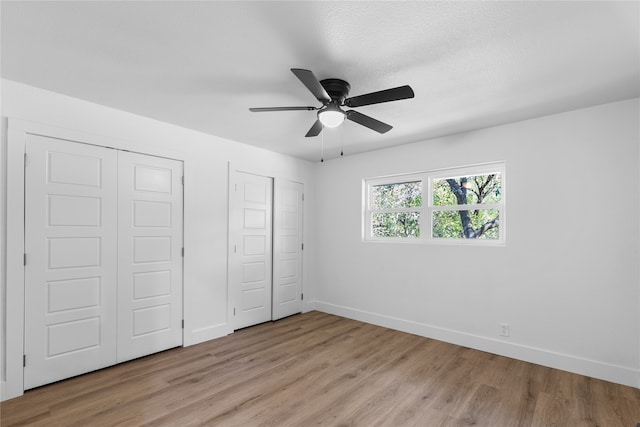 unfurnished bedroom with light hardwood / wood-style flooring, a textured ceiling, two closets, and ceiling fan