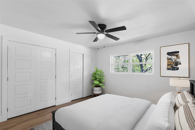 bedroom featuring dark hardwood / wood-style floors, two closets, a textured ceiling, and ceiling fan