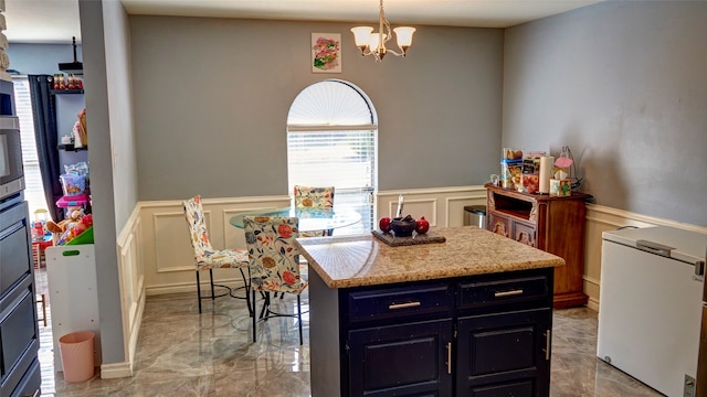 kitchen featuring a kitchen island, a chandelier, fridge, pendant lighting, and light stone counters