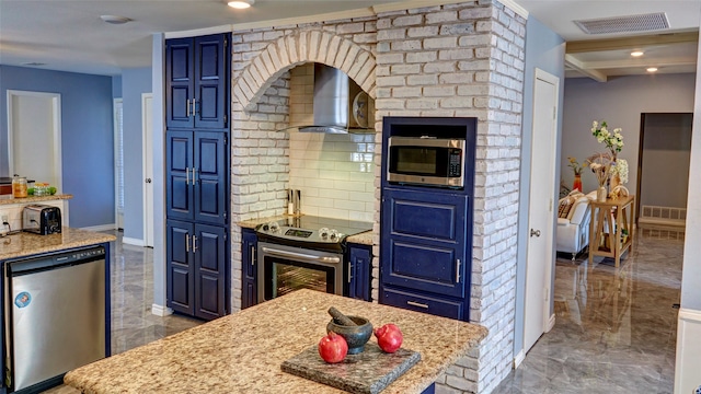 kitchen featuring wall chimney range hood, blue cabinetry, light stone countertops, and stainless steel appliances