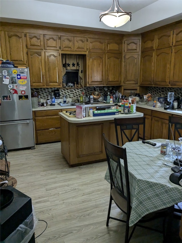 kitchen with hanging light fixtures, backsplash, a breakfast bar, stainless steel refrigerator, and light hardwood / wood-style flooring