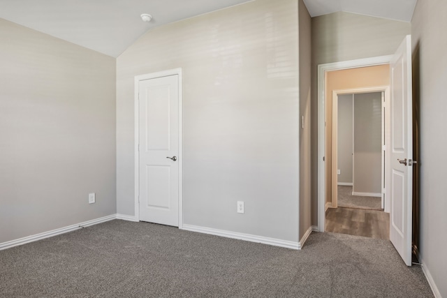 unfurnished bedroom with vaulted ceiling and dark carpet