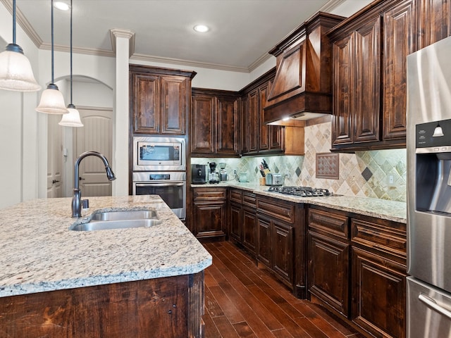 kitchen featuring custom exhaust hood, hanging light fixtures, appliances with stainless steel finishes, dark brown cabinetry, and sink