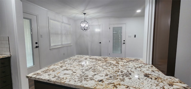 interior space featuring an inviting chandelier, ornamental molding, light stone countertops, and decorative light fixtures