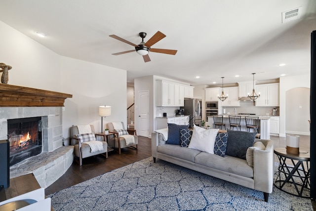 living room featuring a stone fireplace, dark hardwood / wood-style floors, and ceiling fan with notable chandelier