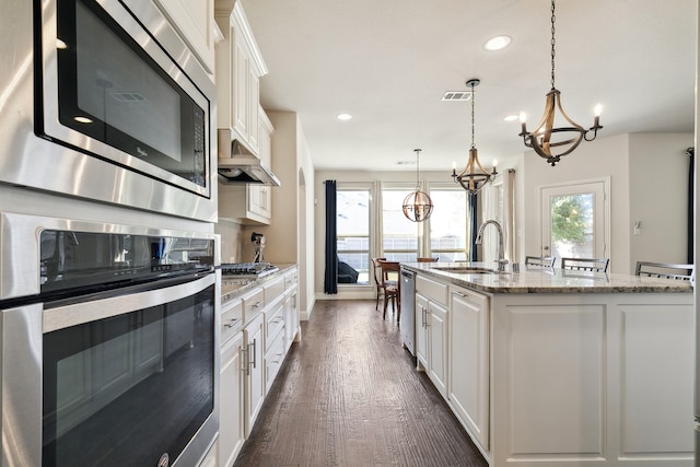 kitchen featuring appliances with stainless steel finishes, decorative light fixtures, white cabinetry, and an island with sink