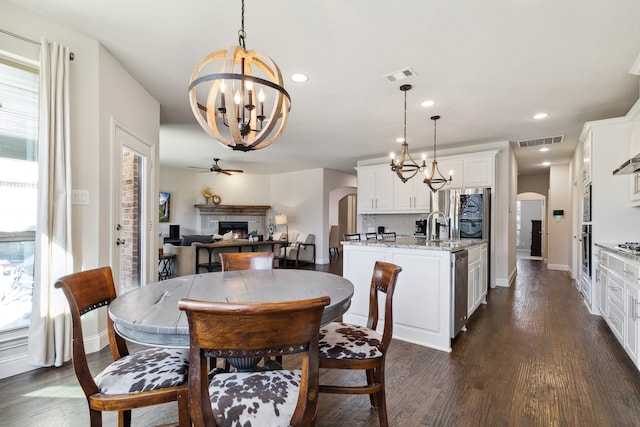 dining room with ceiling fan with notable chandelier, sink, a tile fireplace, and dark hardwood / wood-style floors