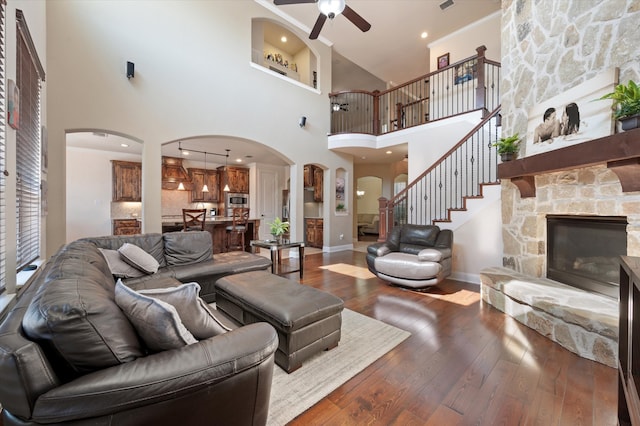 living room featuring a towering ceiling, a stone fireplace, wood-type flooring, and ceiling fan