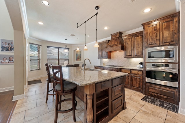 kitchen with an island with sink, sink, crown molding, custom exhaust hood, and appliances with stainless steel finishes