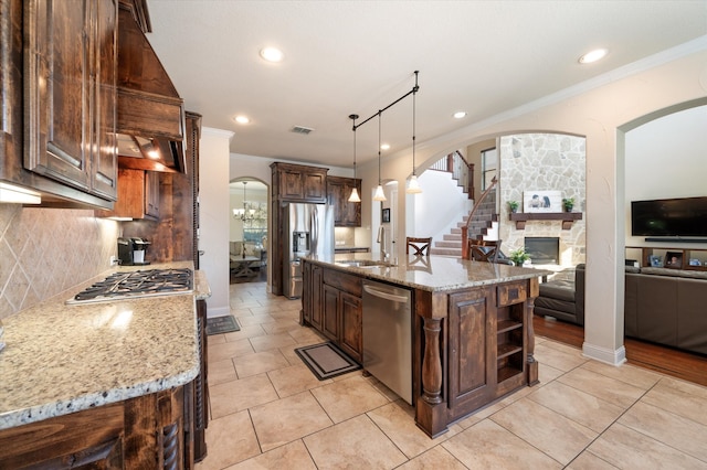 kitchen featuring an island with sink, hanging light fixtures, stainless steel appliances, light stone countertops, and tasteful backsplash