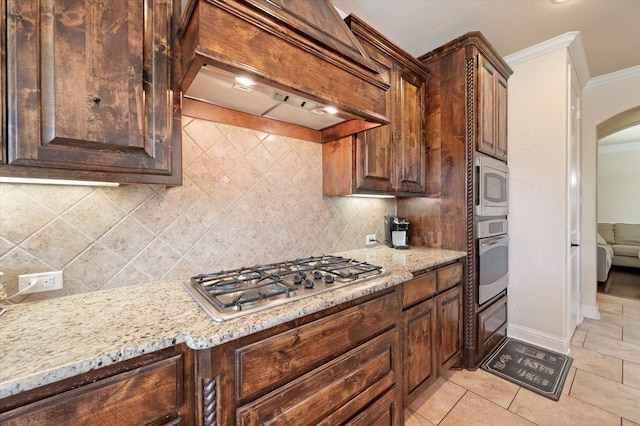 kitchen featuring backsplash, premium range hood, light stone countertops, ornamental molding, and stainless steel appliances