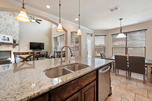 kitchen featuring sink, a fireplace, ceiling fan, decorative light fixtures, and light stone counters