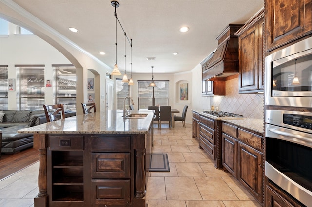 kitchen featuring dark brown cabinets, a center island with sink, a wealth of natural light, sink, and light stone countertops