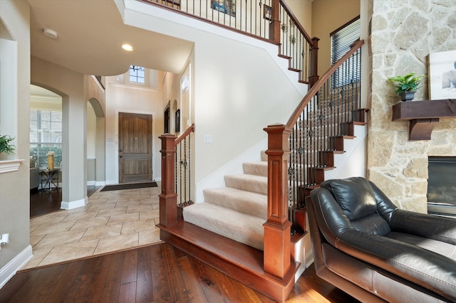 foyer entrance featuring a towering ceiling, a stone fireplace, and light wood-type flooring